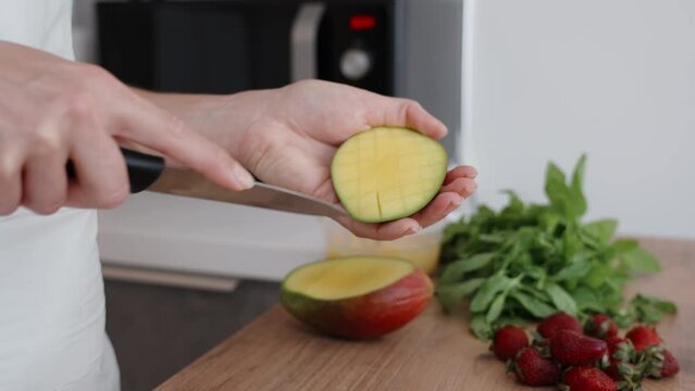 A woman cuts mango into cubes, with strawberries and mint nearby. Slow motion.