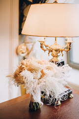Wedding. Details. Bride's bouquet of white roses with ribbon on the table in the hotel room next to a vintage lamp
