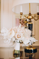 Wedding. Details. Bride's bouquet of white roses with ribbon on the table in the hotel room next to a vintage lamp