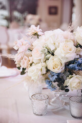 Wedding. Decor. Floristics. The festive table is decorated with a composition of pink and blue flowers with leaves of greenery. There are candles, glasses and plates on the table