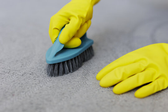 close up of hands in yellow rubber gloves cleaning carpet with brush
