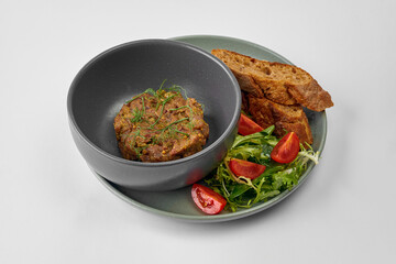 Beef tartare with salad and baguette in a bowl on a gray background