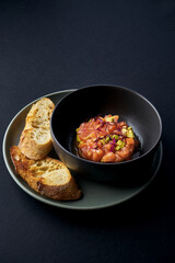 Beef tartare with salad and baguette in a bowl on a black background