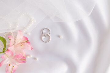 Gentle wedding background. Two wedding rings made of platinum with diamonds on white satin...