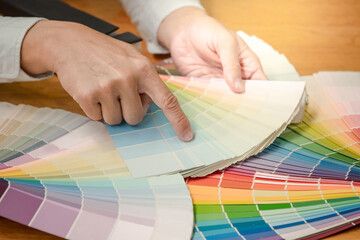 Designer hand choosing and pointing at color swatch samples catalog or rainbow colour palette guide...