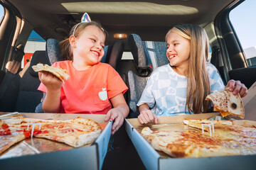 Portrait of two positive smiling sisters eating Huge just cooked italian pizzas sitting in child...