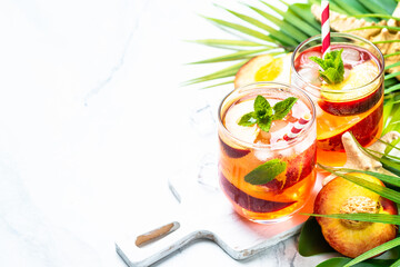 Peach cocktail, iced peach tea, fruit drink with palm leaves at tropical background.