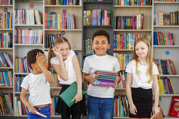 Four children holding stack of books in library. Multiethnic classmates having fun. Back to school.