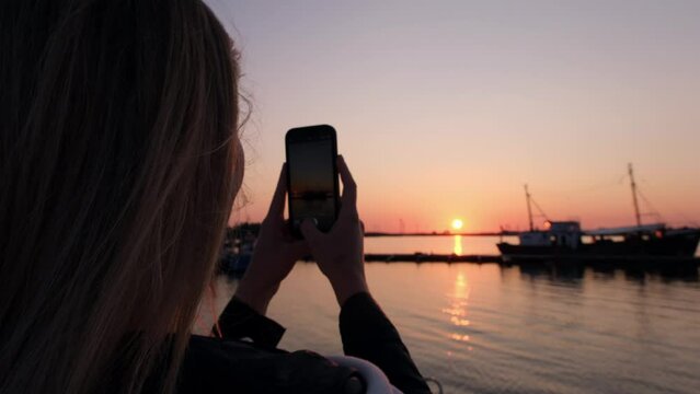 Sunset photography adventure. A girl capturing the serene beauty of a ship. The tranquil scene as she composes the perfect shot with a phone against the backdrop of a peach-colored sky.