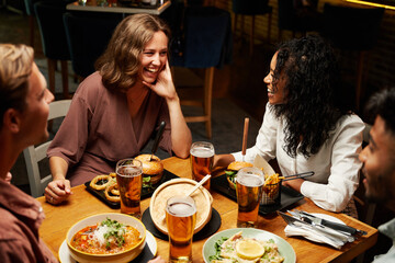 Happy young multiracial group of friends in casual clothing smiling during conversation over dinner