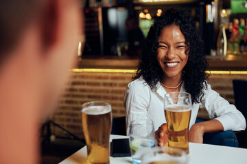 Young multiracial friends in casual clothing smiling while enjoying beers at restaurant