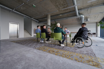 Fototapeta na wymiar A diverse group of business professionals, including an person with a disability, gathered at a modern office for a productive and inclusive meeting.