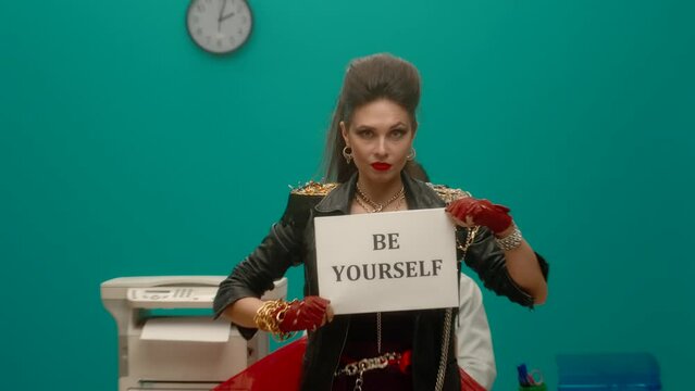 The female freak holds a sheet of paper with words BE YOURSELF and then scatters them. Woman in a black leather jacket with chains in the office. Feminism. Girl power. Advertising. Slow motion.