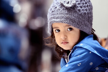 2 years old cute and adorable Asian Indian baby girl wearing grey woolen cap and blue jacket sitting and looking at the camera innocently