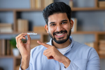 Young arab man with beard wearing casual clothes holding an invisible braces aligner and pointing...