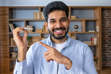 Young arab man with beard holding invisible aligner orthodontic and braces and pointing at it, recommending this new treatment. Dental healthcare concept.
