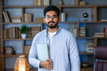 Smiling IT worker in blue shirt look at camera holding laptop at office. concept of remote and freelance work. millennial successful man in glasses