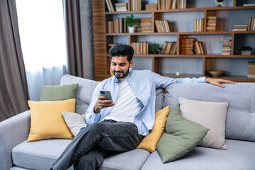 indian millennial bearded man using smart phone for scrolling social media at home