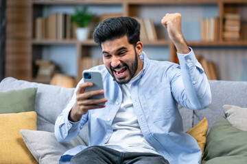 Excited overjoyed indian man winner holding smartphone feeling euphoric with mobile online bet bid...