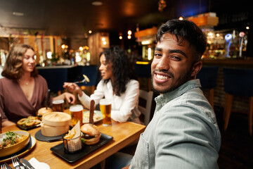 Happy young multiracial group of friends in casual clothing eating dinner at restaurant