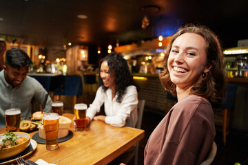 Young multiracial group of friends in casual clothing smiling around table at restaurant