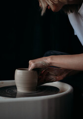 Close up girl ceramist works behind a potter's wheel in profile on a dark background