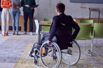 A group of diverse entrepreneurs gather in a modern office to discuss business ideas and strategies, while a colleague in a wheelchair joins them.