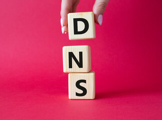 DNS -Domain Name Server - Consumer Price Index symbol. Concept word DNS on wooden cubes. Businessman hand. Beautiful red background. Business and DNS concept. Copy space.