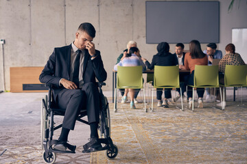 A melancholic businessman in a wheelchair sitting with a sad expression, gazing through the window of a modern office, conveying a sense of solitude
