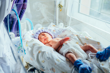 Premature newborn recovering in incubator. His foot in a blue sock with a premature infant pulse oximeter. Intensive care unit, ventilator.