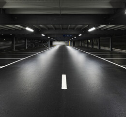 Obraz premium Modern underground garage with lamps illuminating the scene. Parking lines are drawn on the floor.