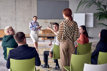 A group of young business professionals in a modern office attentively listens to colleague...