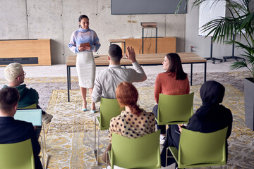 A group of young business professionals in a modern office attentively listens to colleague...