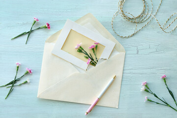 Envelope and self made greeting card concept with fresh carnation flowers. Wrapped gift, paper postcard, paper envelope, cord, scissors and purple carnations.