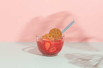Minimal scene glass bowl with strawberry smoothie and diet biscuit. Healthy meal for a happy day. Concept with a shadow on a blue and pink background.