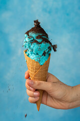 mano sosteniendo un cono de helado de color azul sobre un fondo azul con espacio para copy  da la sensacion de refrescante - obrazy, fototapety, plakaty