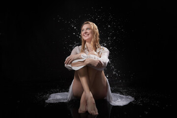 Beautiful sexy skinny girl in a dark hall with splashes of water. Female Model blonde woman posing with water on a black background in the studio