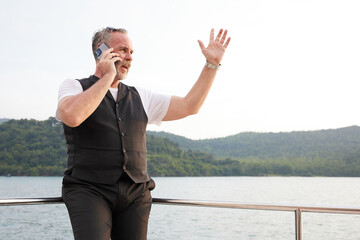 Fototapeta elderly man talking by smartphone and raise hand pose in luxury yacht obraz