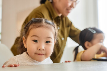 Portrait of Asian little girl looking at camera while sitting at table and waiting for the dinner