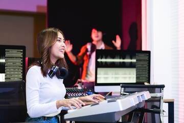 Fototapeta premium Asian producer woman in white shirt playing piano in sound studio with warm lighting background, Happy female music composer artist.