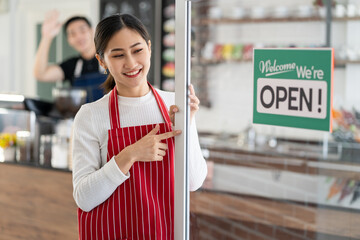 Portrait of woman owner standing at her coffee shop gate with showing open signboard