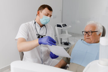 At the dentist charismatic dentist man explain to his patient how the implant are fixed old man sitting on the dentist chair and listening