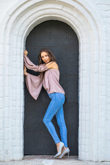 Portrait of a young beautiful brunette girl in blue jeans posing in a stone arch