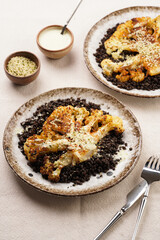 A white plate with brown rim with black beluga lentils and roasted cauliflower with paprika and black pepper seasoning, tahini dressing, on linen table cloth, a delicious high protein vegan meal