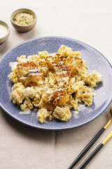 A blue plate with cooked millet and roasted cauliflower with paprika and black pepper seasoning, tahini dressing, on linen table cloth, a delicious gluten free vegan meal