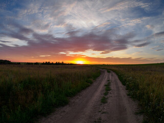 Sunset in the field, dirt road. colorful sky