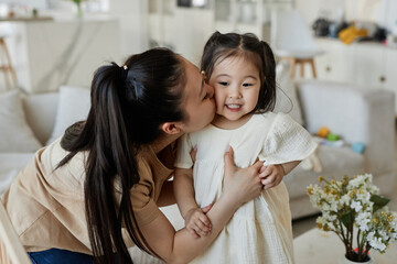 Asian happy mom kissing her little daughter while they playing in the living room