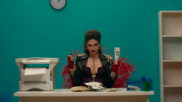 A woman in a black leather jacket, with chains sits at a table in the office, holding money in her hand. The girl brings a gasoline lighter to a dollar bill, sets it on fire. Advertising. Slow motion.