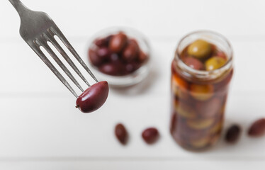 Close-up of olives on fork and glass jar on the kitchen table. pitted green olives in jar.Pickled olives in glass jar. On a wooden background.Marinaded olives. Space for text.Space for copy. Vegan foo
