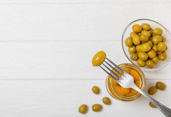 Close-up of olives on fork and glass jar on the kitchen table. pitted green olives in jar.Pickled olives in glass jar. On a wooden background.Marinaded olives. Space for text.Space for copy. Vegan foo